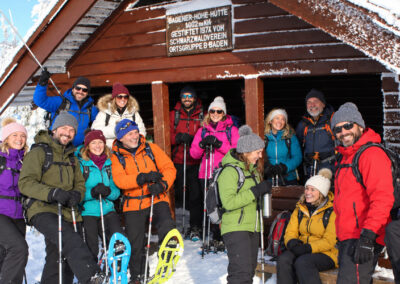 Schneeschuhtour: Gruppe mit Schneeschuhen und Trekkingstöcken vor einer verschneiten Hütte.