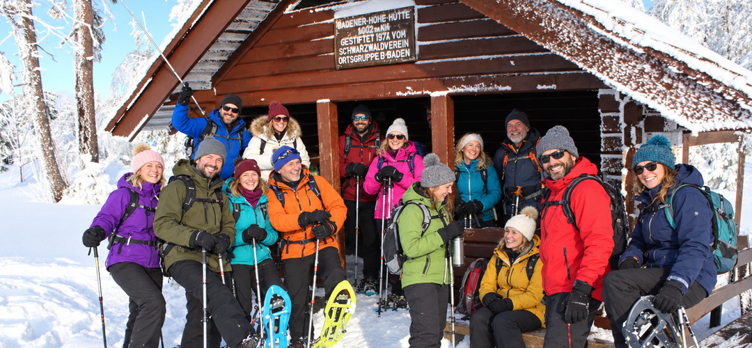 Schneeschuhtour: Gruppe mit Schneeschuhen und Trekkingstöcken vor einer verschneiten Hütte.