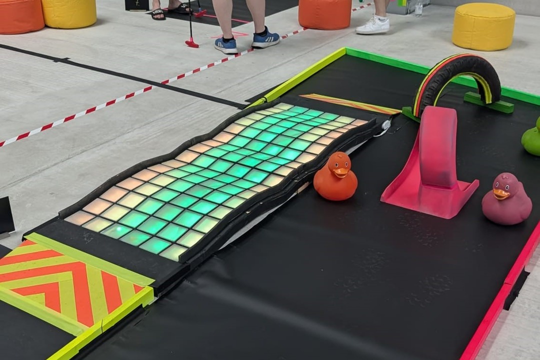 Farbenfrohe Indoor-Golfbahn mit beleuchteten Spielfeldern, bunten Hindernissen und Gummienten als kreative Spielstation für ein abwechslungsreiches Firmenevent.