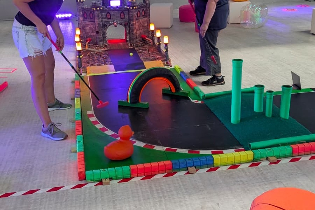 Teilnehmerin beim Indoor-Golf auf einer farbenfrohen Spielbahn mit Burgkulisse, beleuchteten Hindernissen und kreativen Spielstationen – abwechslungsreicher Spielspaß für Firmen- und Teamevents.